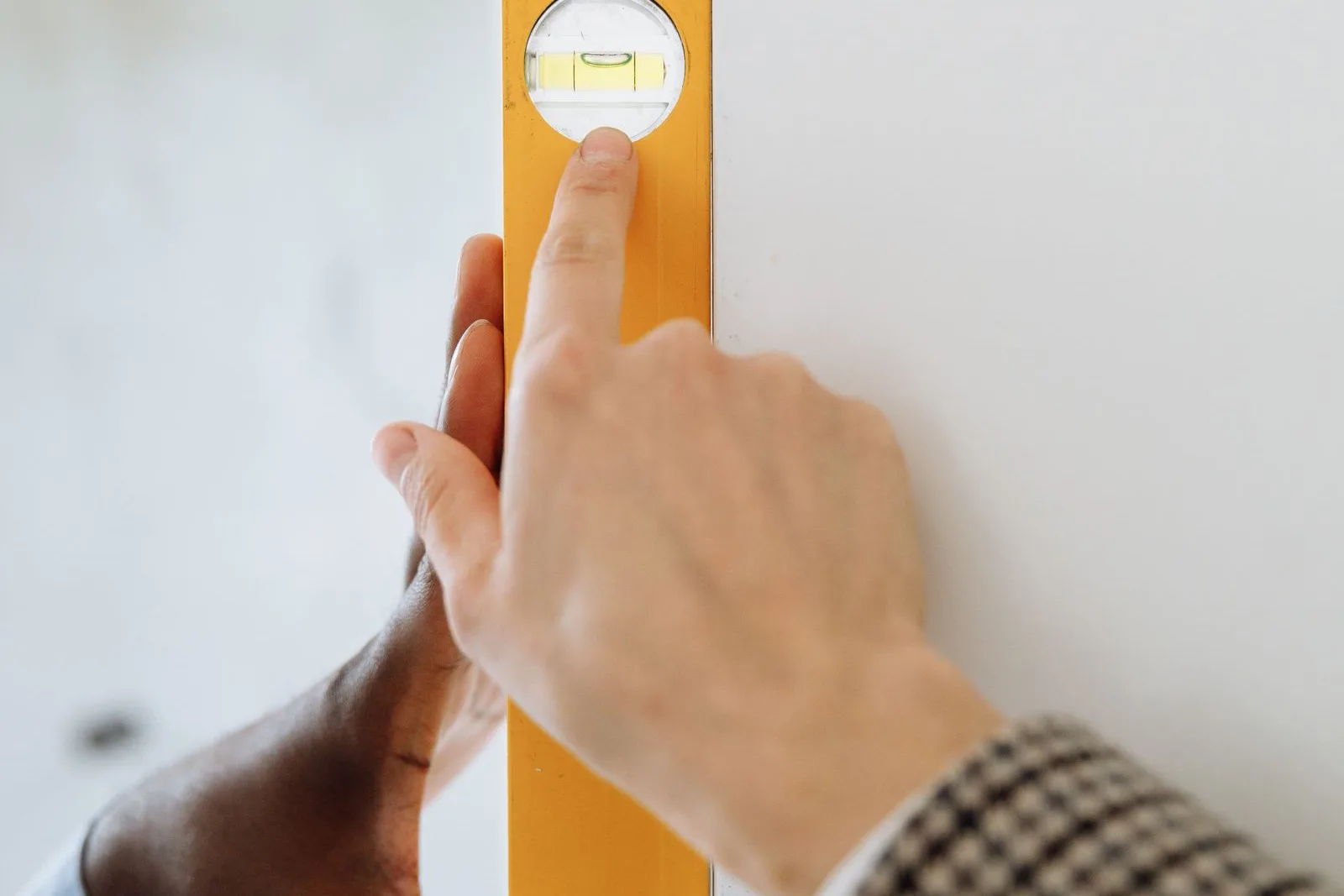 Hands holding a level against a white wall to square up a mini split mounting plate