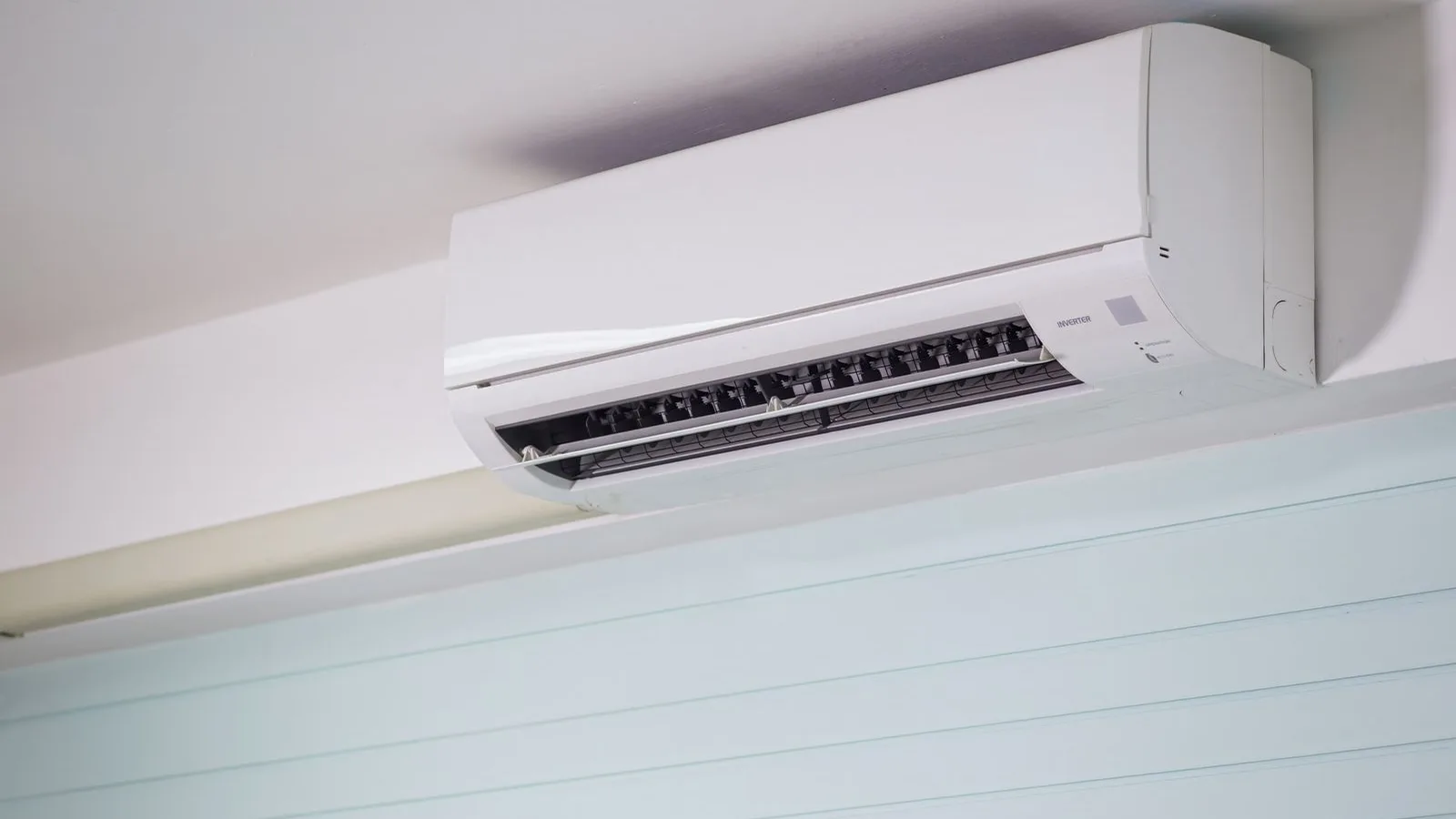 White ductless mini split air conditioner mounted on wall near ceiling with front panel open showing vents and INVERTER label, a helpful visual for any ductless mini split installation guide