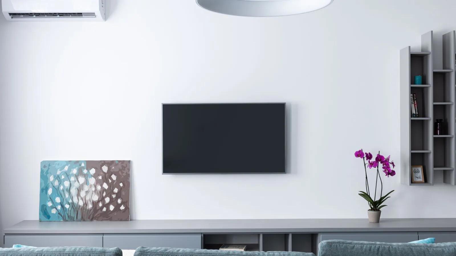White mini split indoor unit placement high on a living room wall above gray furniture and a TV