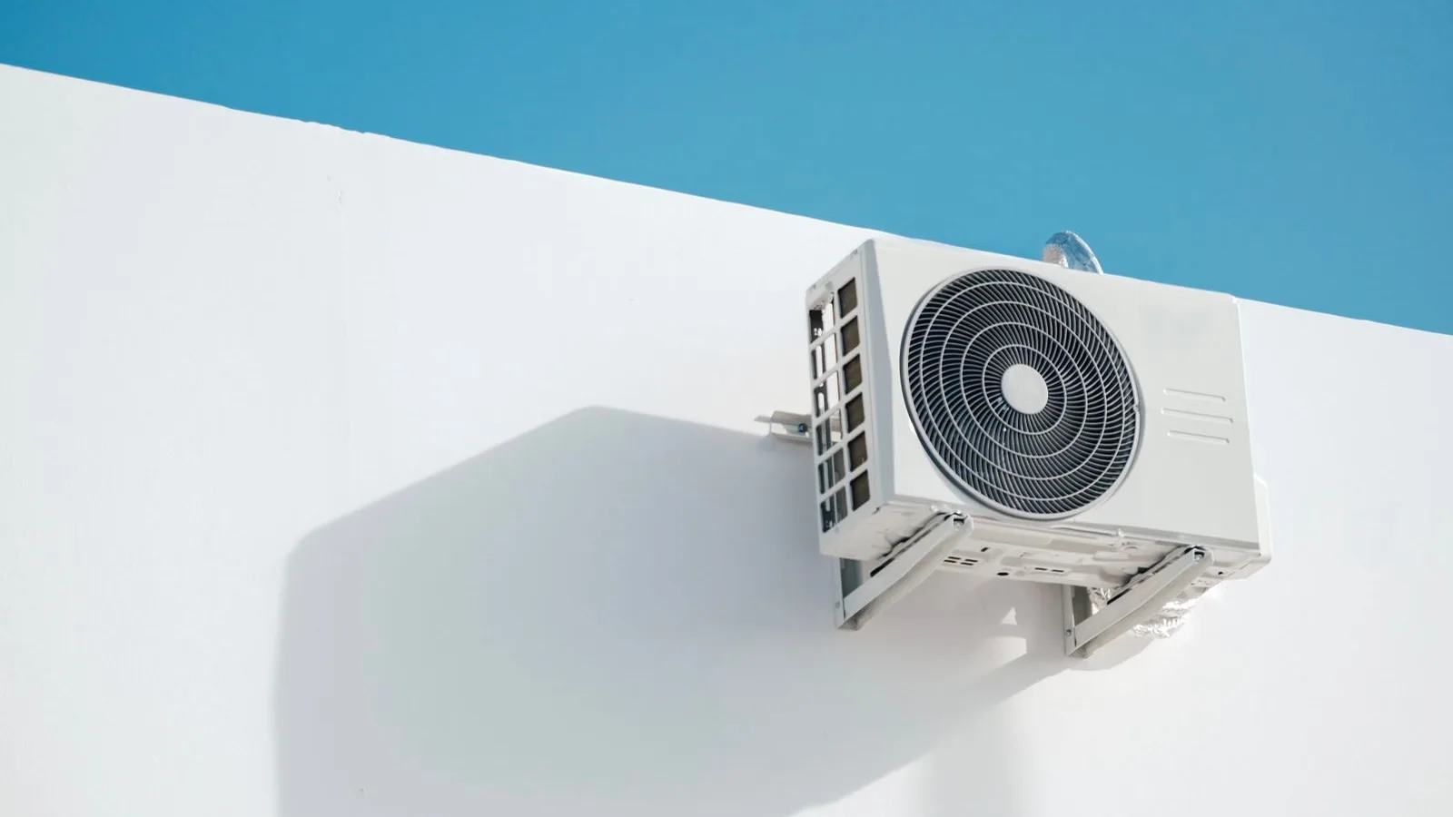 Outdoor mini split condenser placement on a wall bracket with proper side and rear clearance against a white wall