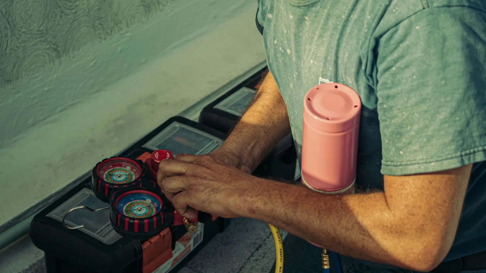 Technician kneels beside a black toolbox with tools for installing a mini split, including a red and black manifold gauge set connected to yellow and blue charging hoses