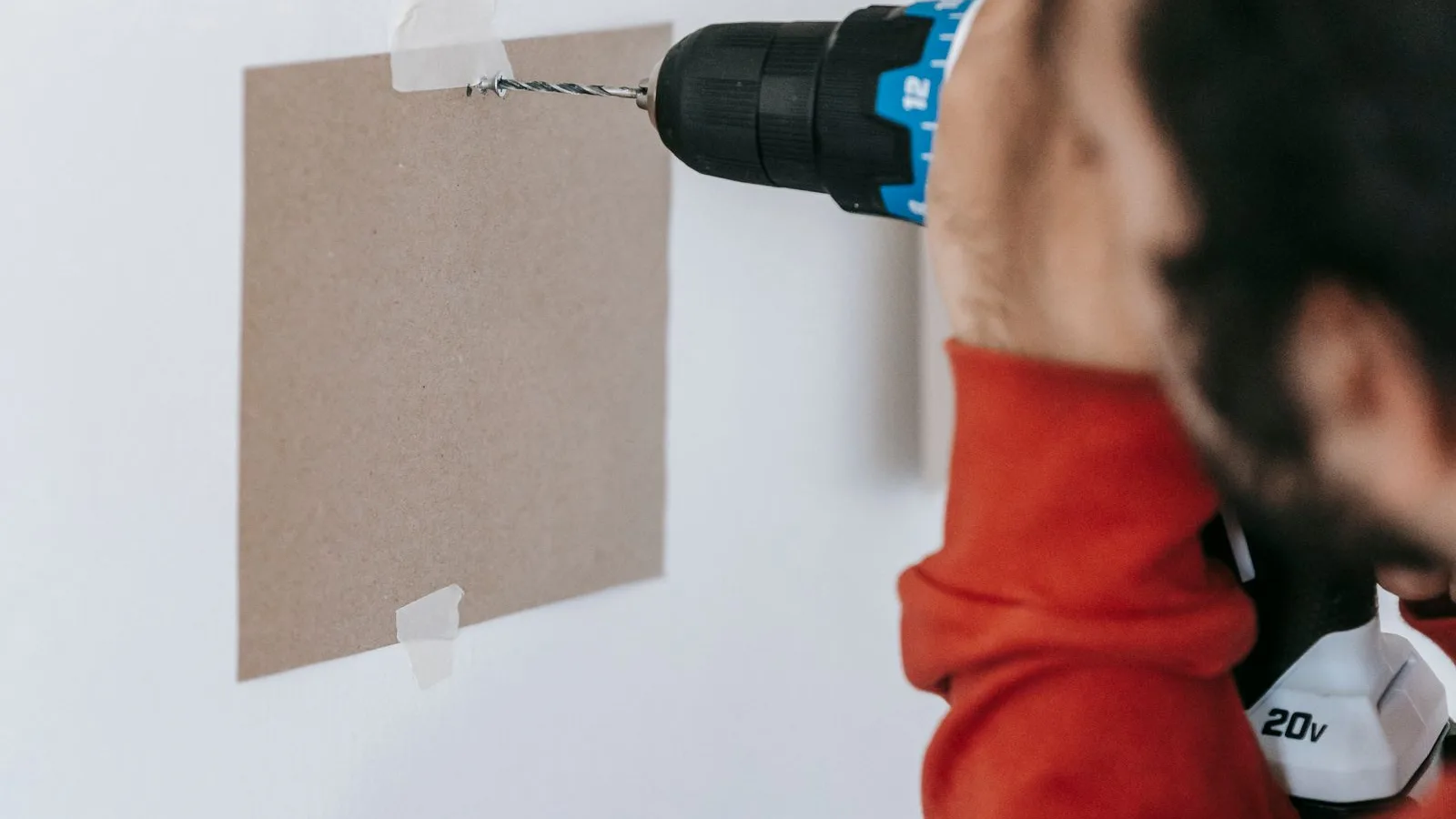 Person using a cordless drill to make a drilling mini split hole through siding taped to a white wall