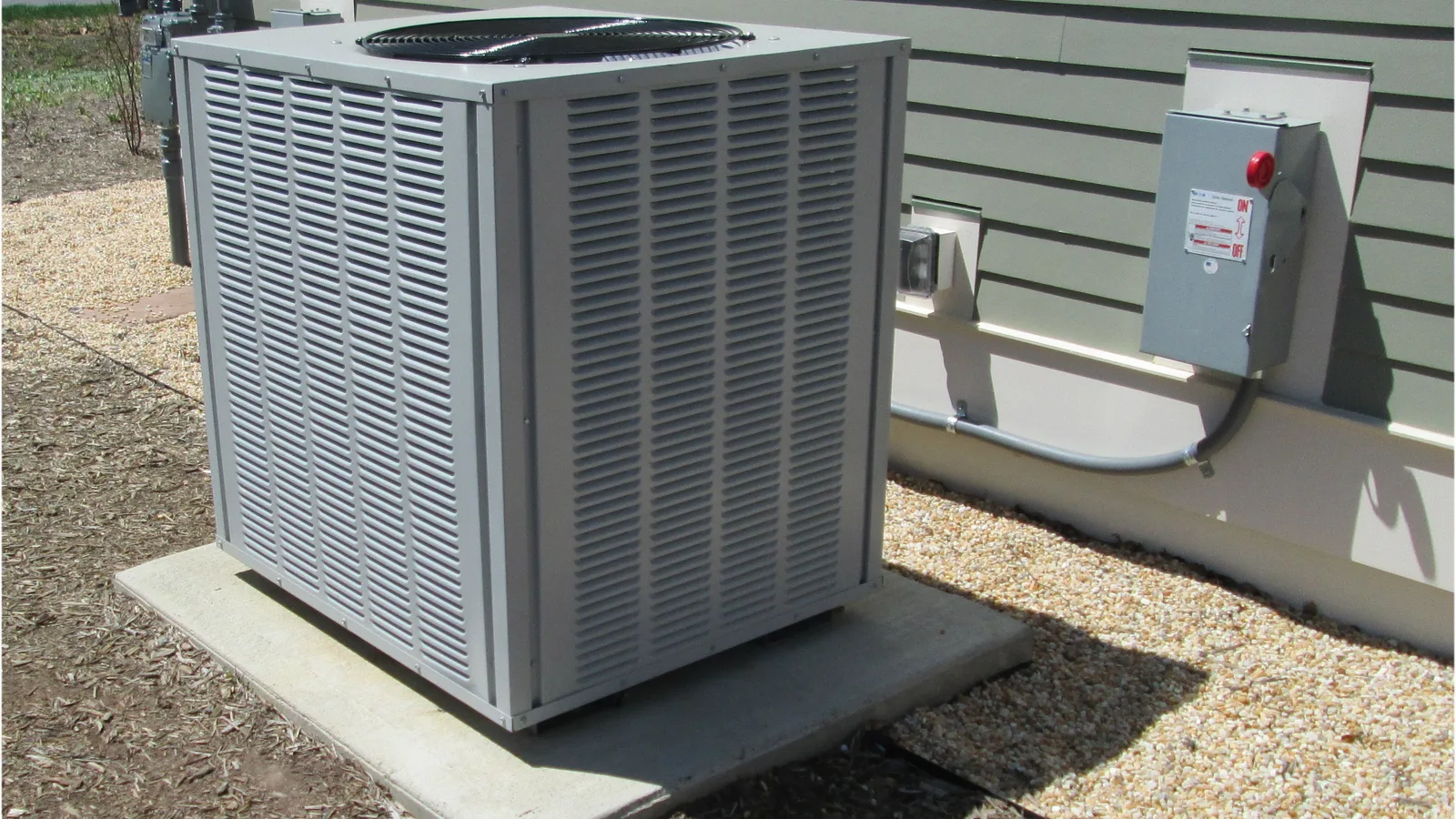 Outdoor condenser unit on a concrete pad beside a house, illustrating a mini split ground stand installation guide