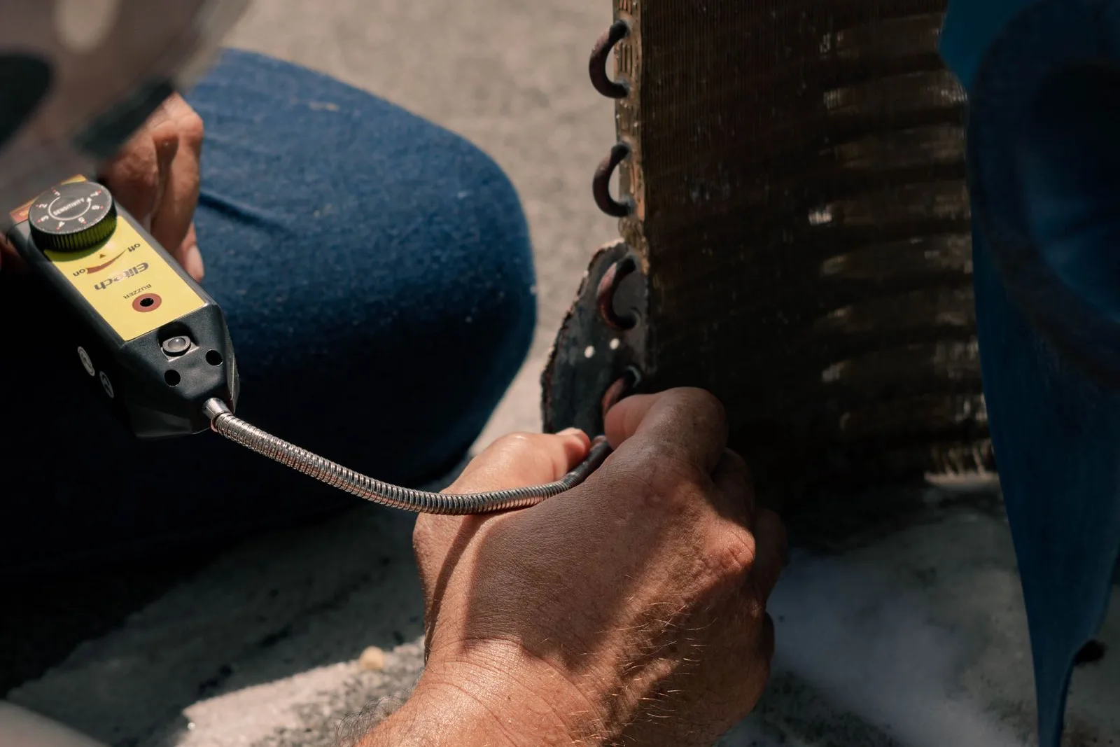 Technician checking a condenser coil with an electronic refrigerant leak detector