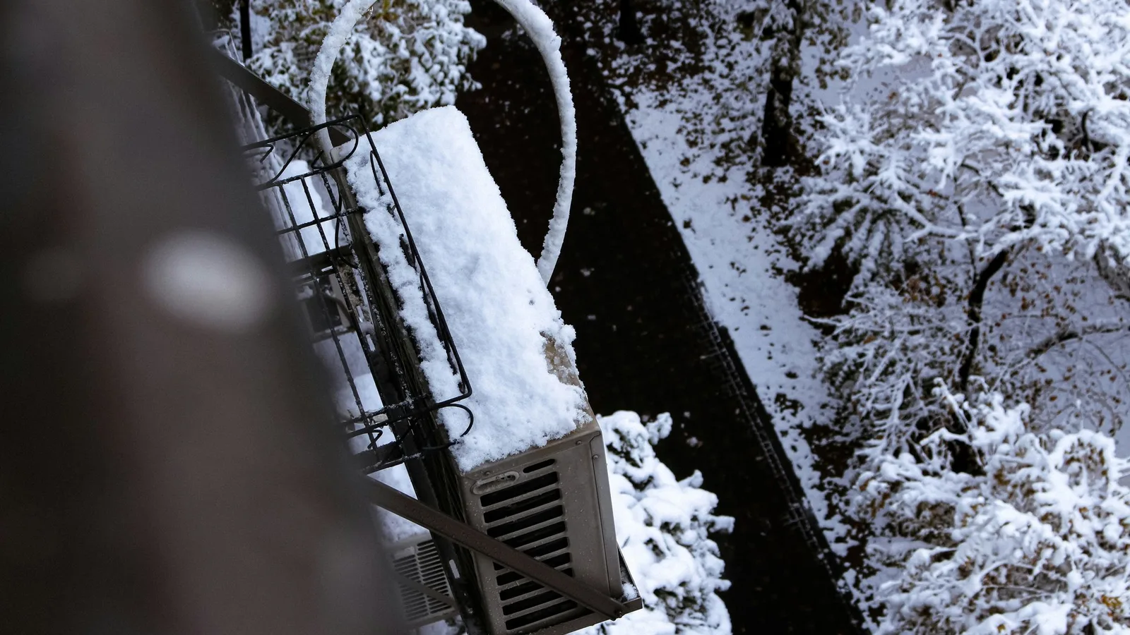 Outdoor mini split condenser unit on a wall bracket with snow, demonstrating outdoor unit placement for mini splits