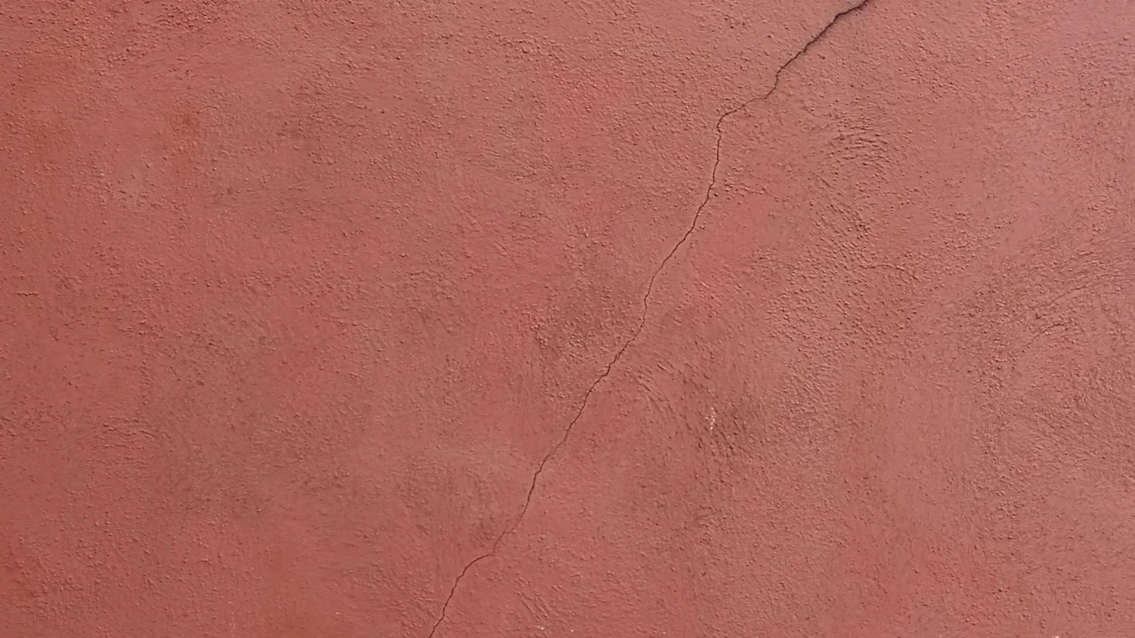 Terracotta stucco wall with a PVC pipe penetration showing an unsealed gap and crack, demonstrating the need for sealing a mini split wall penetration