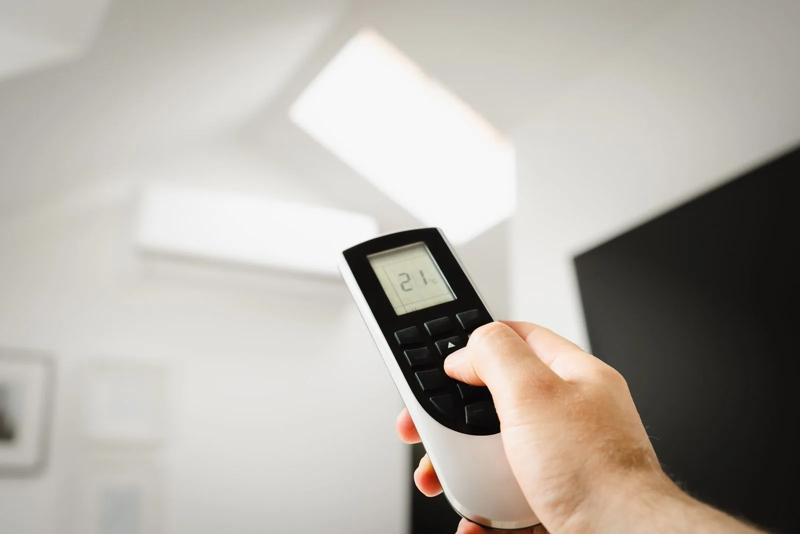 Hand pointing a mini split remote at the indoor unit